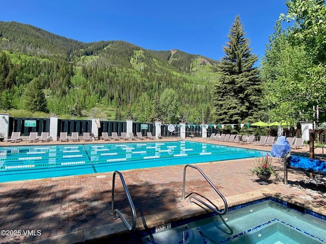 pool featuring a community hot tub, a view of trees, fence, a mountain view, and a patio area