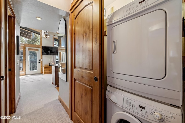 laundry area with ceiling fan, light colored carpet, laundry area, stacked washing maching and dryer, and a textured ceiling