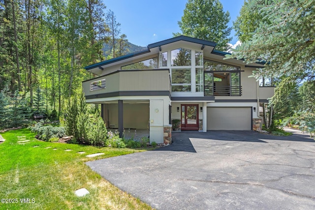 4916 Juniper Ln, Vail, CO 81657 - modern home featuring a balcony, a garage, asphalt driveway, stone siding, and a front lawn
