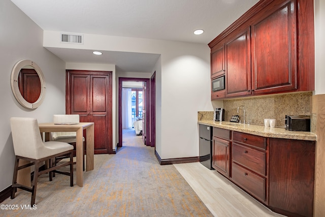 kitchen with black appliances, sink, backsplash, light hardwood / wood-style floors, and light stone counters