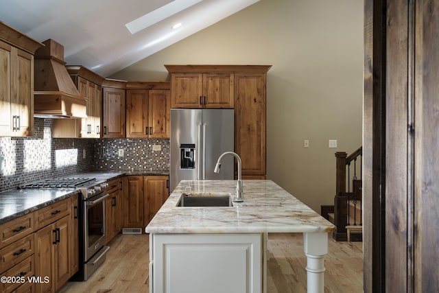 kitchen with vaulted ceiling with skylight, high quality appliances, sink, custom exhaust hood, and a kitchen island with sink