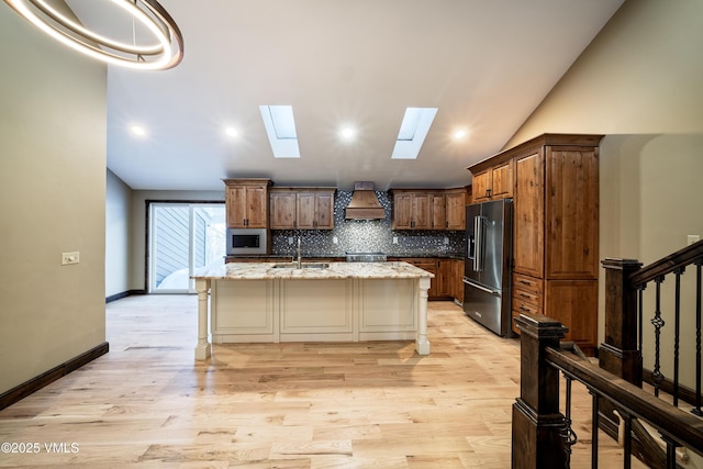 kitchen featuring premium range hood, a breakfast bar, sink, a center island with sink, and high quality fridge