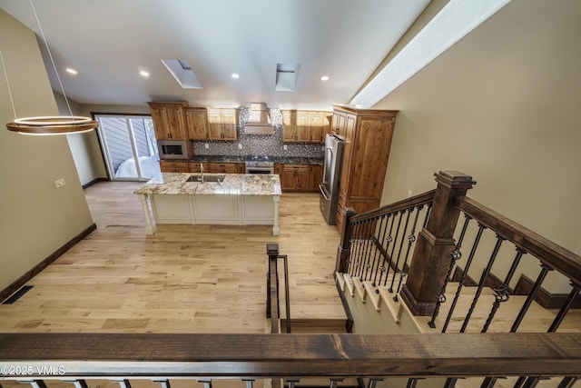 kitchen featuring a skylight, tasteful backsplash, stainless steel fridge, a kitchen breakfast bar, and light stone counters