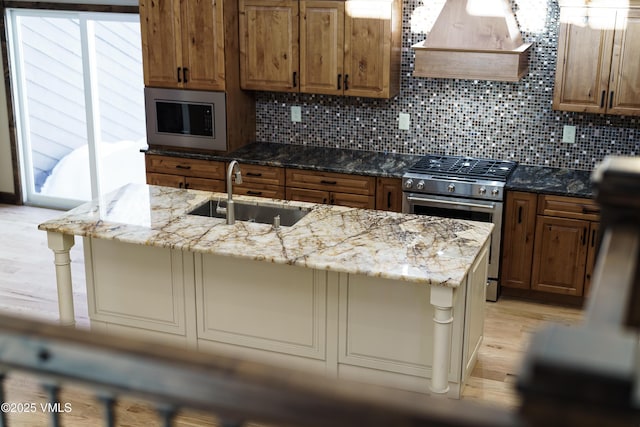 kitchen with appliances with stainless steel finishes, sink, custom exhaust hood, light stone counters, and a center island with sink