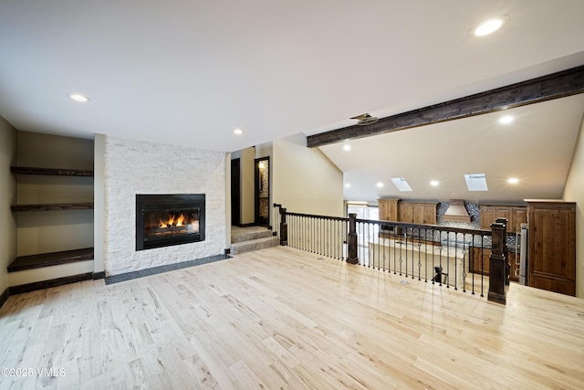 living room featuring lofted ceiling with skylight, a stone fireplace, and light wood-type flooring