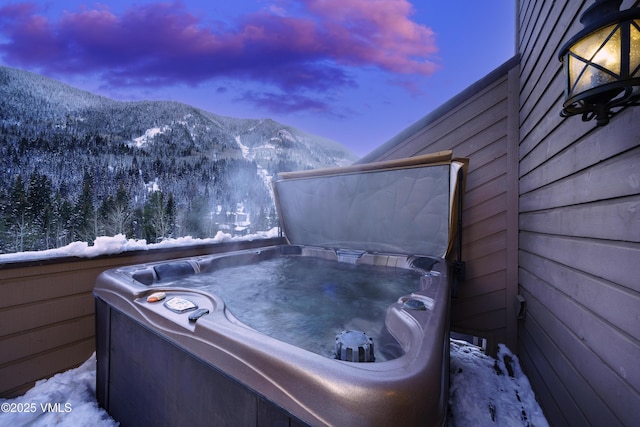 snow covered patio with a hot tub and a mountain view