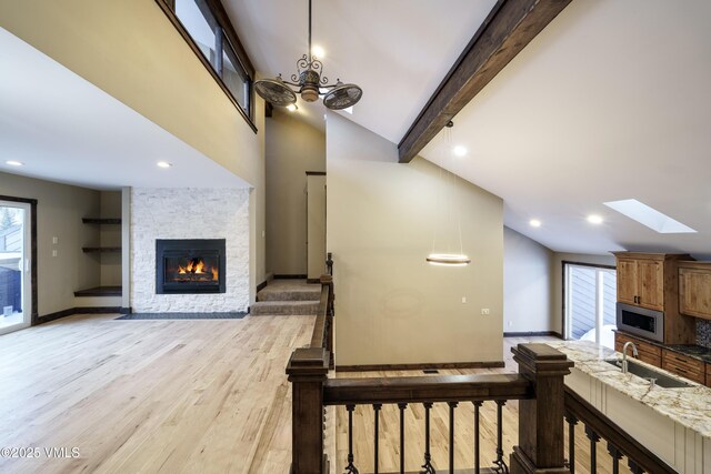 interior space featuring sink, a skylight, a stone fireplace, beamed ceiling, and light wood-type flooring