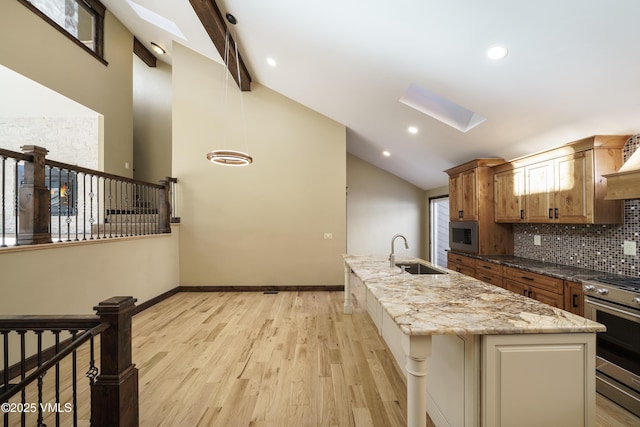 kitchen with sink, a skylight, stainless steel appliances, light hardwood / wood-style floors, and an island with sink