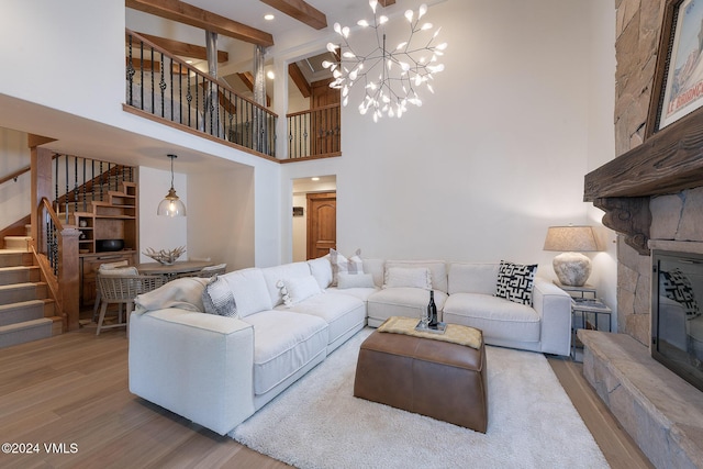 living room with a towering ceiling, an inviting chandelier, a fireplace, wood-type flooring, and beam ceiling