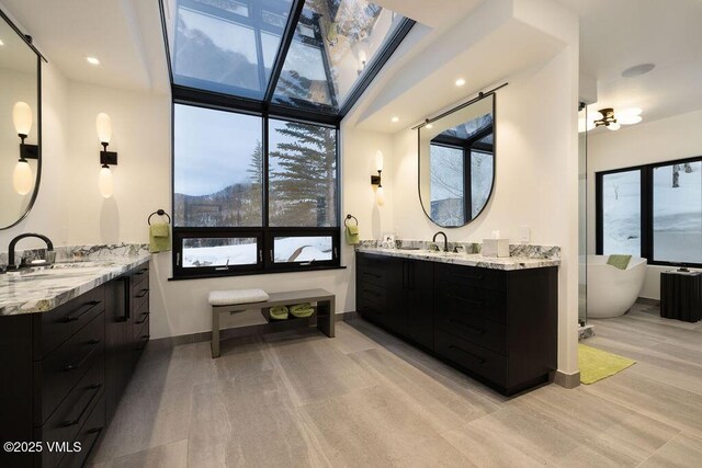 bathroom with a soaking tub, two vanities, a sink, and baseboards