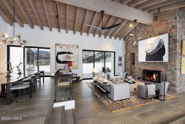 living area featuring wood-type flooring, a stone fireplace, high vaulted ceiling, beamed ceiling, and ceiling fan with notable chandelier