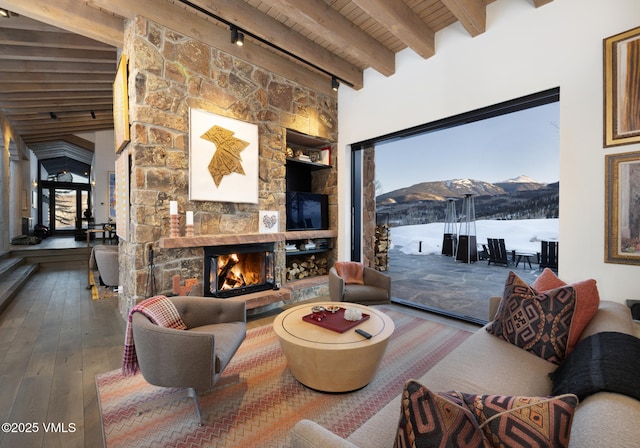 living area with a stone fireplace, wooden ceiling, hardwood / wood-style floors, beamed ceiling, and track lighting