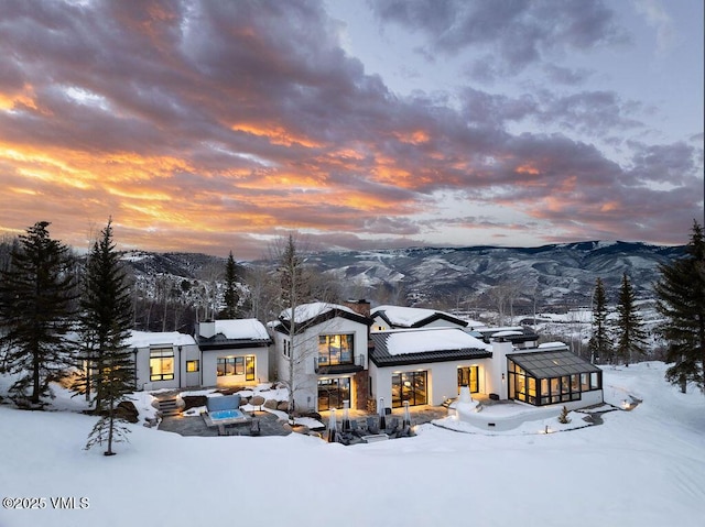 snow covered property featuring a mountain view, a chimney, and stucco siding