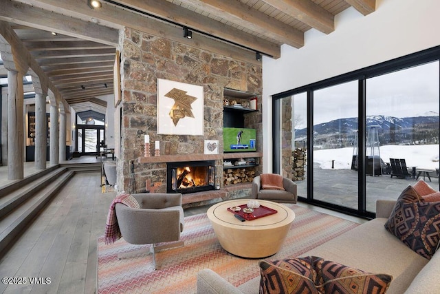 living room with lofted ceiling with beams, hardwood / wood-style flooring, wooden ceiling, rail lighting, and a stone fireplace