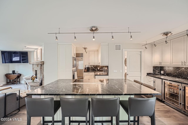 kitchen with wine cooler, a stone fireplace, a breakfast bar area, dark stone counters, and white cabinets