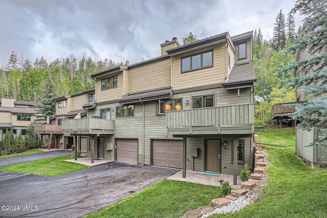 rear view of property with a balcony, a yard, and a garage