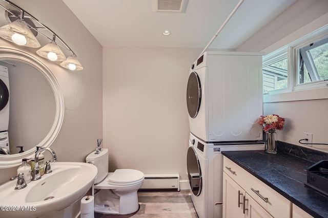 bathroom with stacked washer / drying machine, toilet, sink, a baseboard radiator, and hardwood / wood-style floors