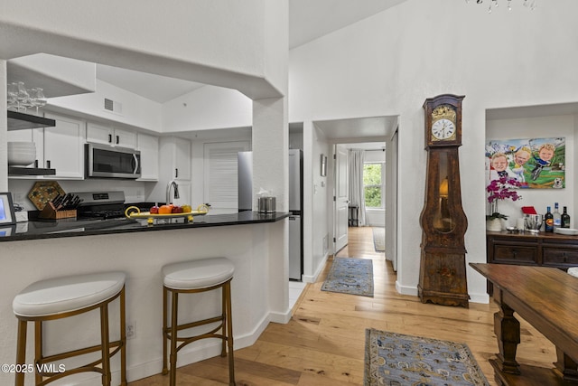 55 River Pines Ct Unit A302, Edwards, CO 81632 - kitchen with appliances with stainless steel finishes, dark countertops, light wood finished floors, white cabinetry, and a peninsula