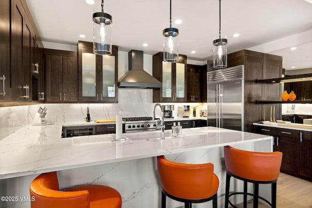 kitchen with built in refrigerator, tasteful backsplash, wall chimney exhaust hood, and light stone countertops