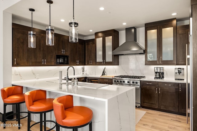 kitchen featuring tasteful backsplash, black microwave, light stone counters, high end range, and wall chimney exhaust hood