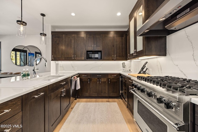 kitchen featuring backsplash, dark brown cabinets, wall chimney range hood, appliances with stainless steel finishes, and a sink