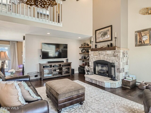 living room with a stone fireplace, hardwood / wood-style floors, and a high ceiling