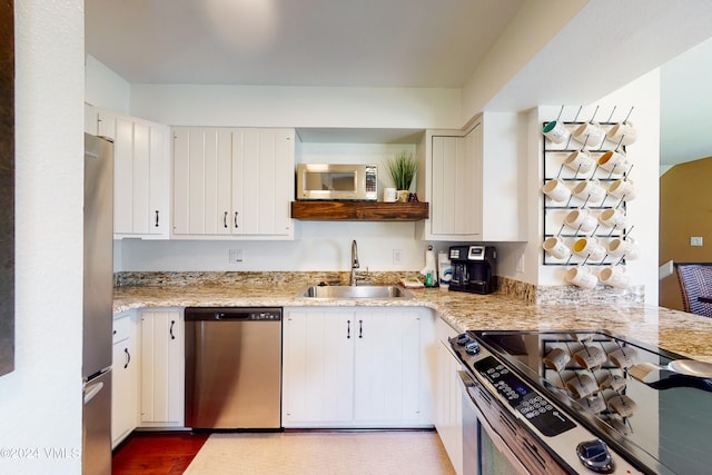 kitchen featuring stainless steel appliances, light stone countertops, sink, and white cabinets