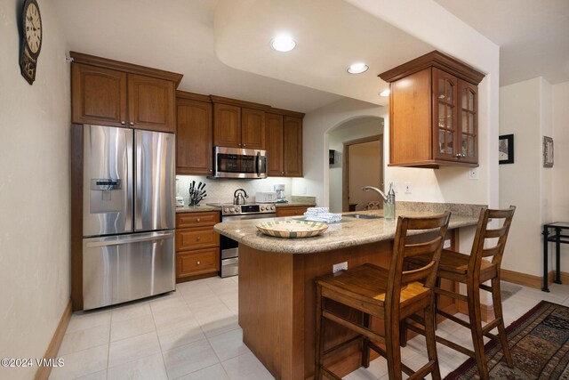 kitchen with appliances with stainless steel finishes, sink, a kitchen bar, decorative backsplash, and kitchen peninsula