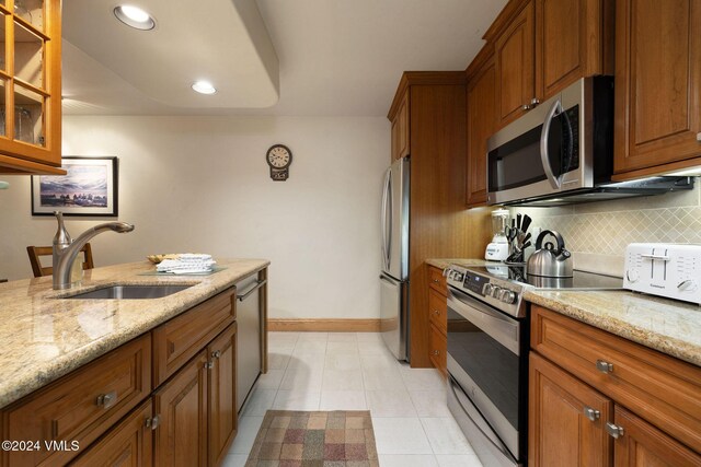 kitchen with light stone countertops, appliances with stainless steel finishes, sink, and backsplash