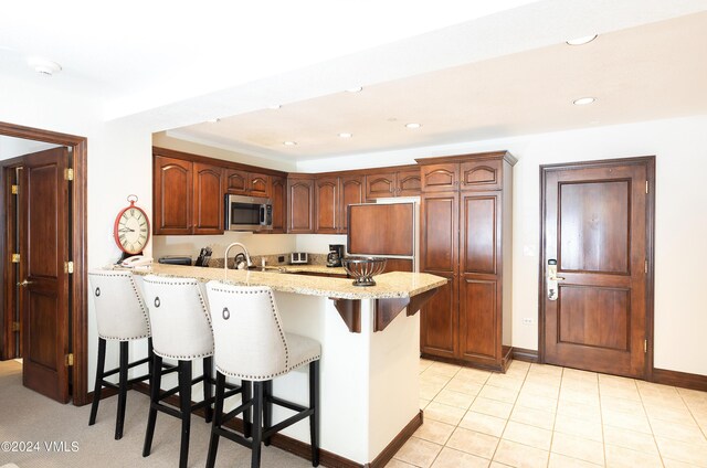 kitchen featuring light stone countertops, light tile patterned floors, a kitchen breakfast bar, and kitchen peninsula