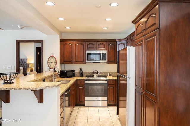 kitchen featuring appliances with stainless steel finishes, sink, a kitchen bar, kitchen peninsula, and light stone countertops