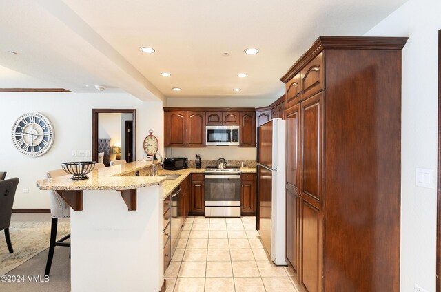 kitchen with light tile patterned flooring, a breakfast bar area, light stone counters, appliances with stainless steel finishes, and kitchen peninsula