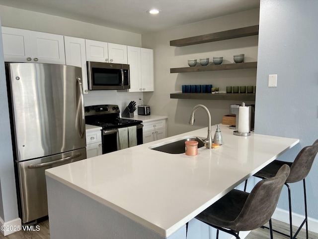 kitchen with wood finished floors, a kitchen breakfast bar, white cabinetry, a sink, and stainless steel appliances