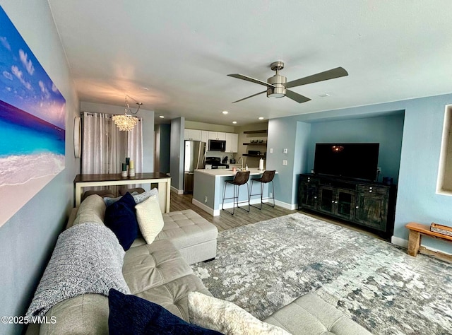 living area with baseboards, recessed lighting, light wood finished floors, and ceiling fan with notable chandelier