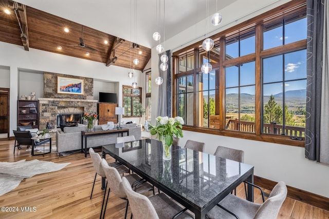 dining area with a stone fireplace, hardwood / wood-style floors, high vaulted ceiling, beamed ceiling, and wooden ceiling