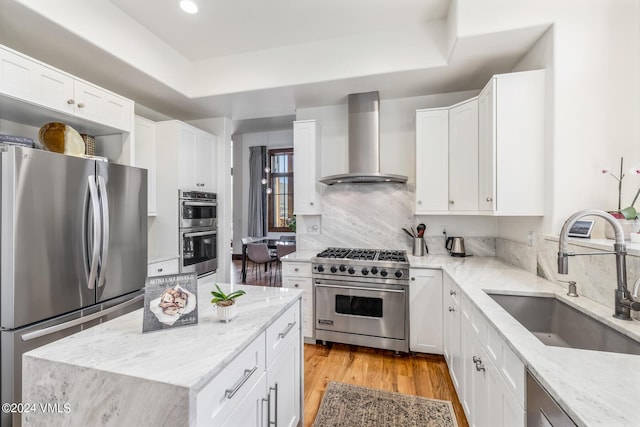 kitchen featuring wall chimney range hood, sink, appliances with stainless steel finishes, white cabinetry, and light stone counters