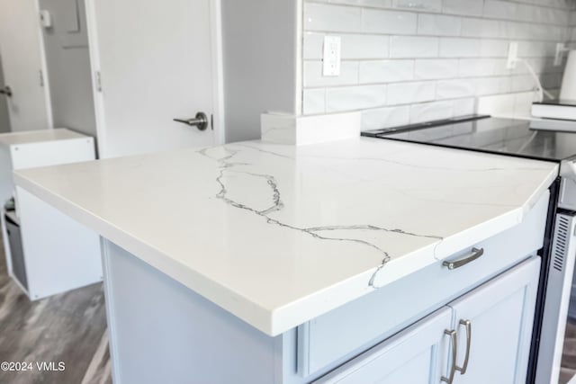 kitchen with tasteful backsplash, light stone countertops, hardwood / wood-style flooring, and white cabinets