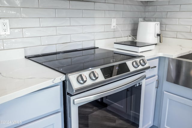 kitchen with light stone counters, stainless steel range with electric stovetop, and backsplash