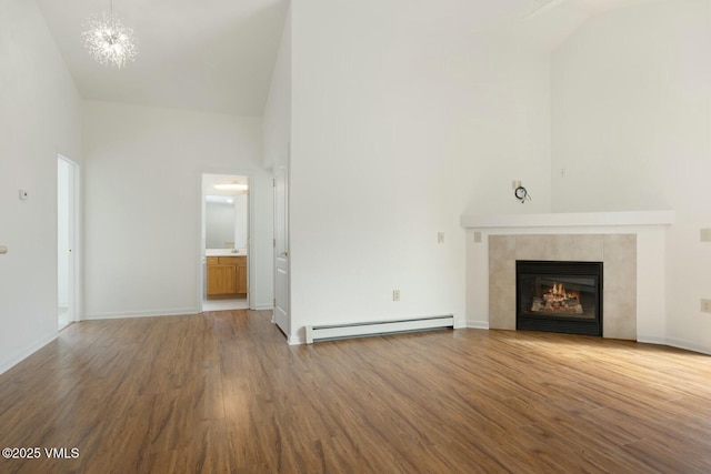 unfurnished living room with a baseboard heating unit, a chandelier, a fireplace, wood finished floors, and high vaulted ceiling