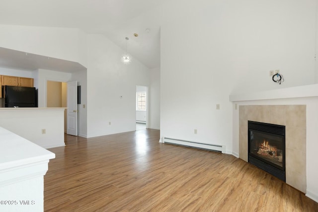 unfurnished living room featuring a baseboard heating unit, light wood finished floors, high vaulted ceiling, and a tile fireplace