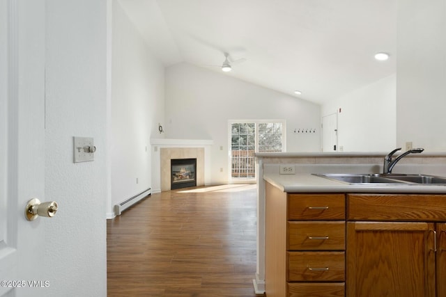 kitchen with brown cabinetry, wood finished floors, lofted ceiling, a sink, and a baseboard heating unit