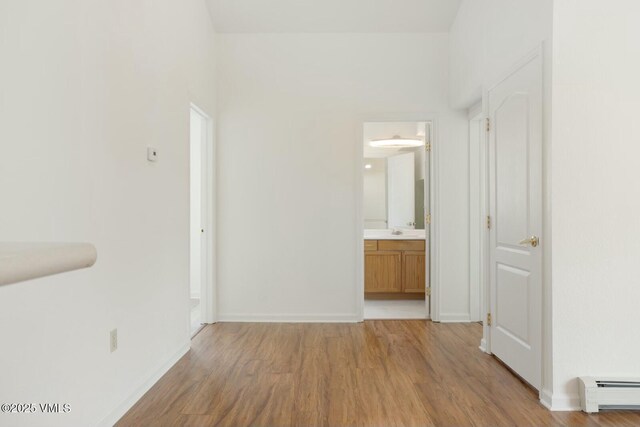 interior space featuring light wood finished floors, baseboards, baseboard heating, and a sink