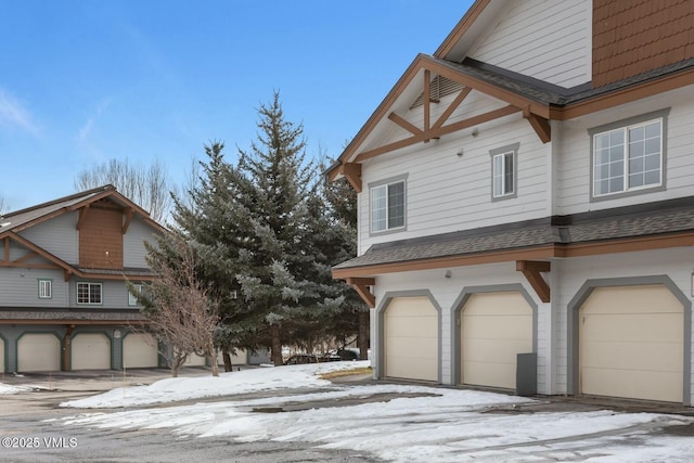 snow covered property with a garage and roof with shingles