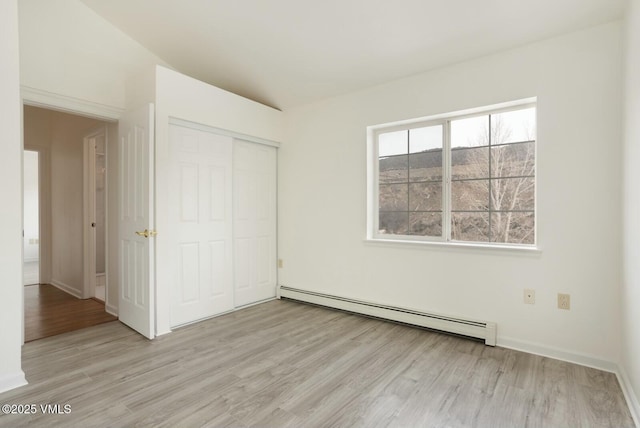 unfurnished bedroom with a baseboard heating unit, light wood-style floors, a closet, and baseboards