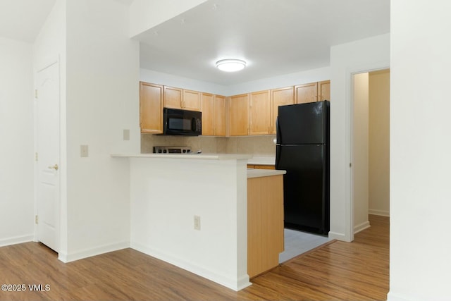 kitchen featuring light brown cabinetry, black appliances, light countertops, light wood-style floors, and tasteful backsplash