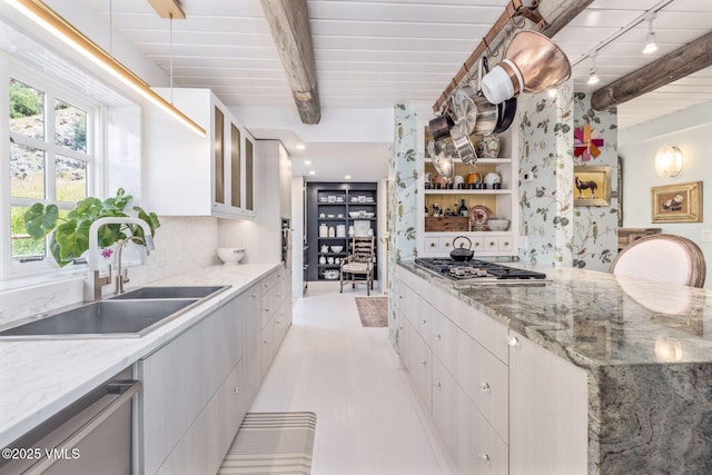 kitchen featuring stainless steel appliances, beam ceiling, light stone countertops, and sink