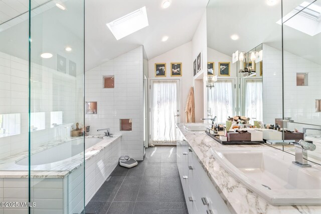 bathroom with lofted ceiling with skylight, tile walls, vanity, a relaxing tiled tub, and tile patterned flooring