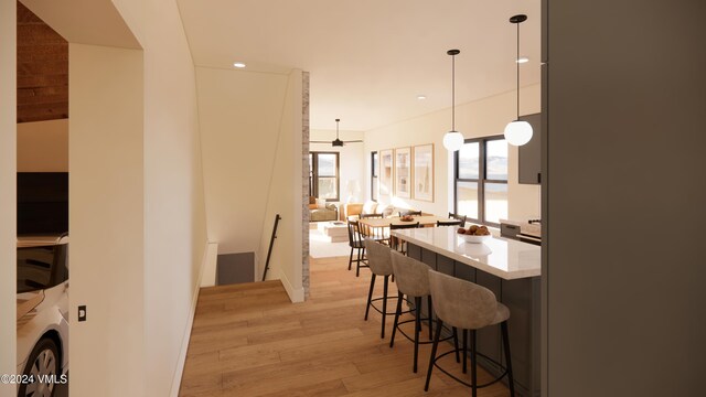 kitchen featuring decorative light fixtures, a breakfast bar, ceiling fan, and light wood-type flooring