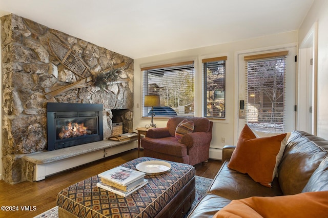 living room featuring dark hardwood / wood-style flooring, a stone fireplace, plenty of natural light, and a baseboard radiator