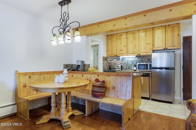 kitchen featuring pendant lighting, appliances with stainless steel finishes, a baseboard heating unit, tasteful backsplash, and light brown cabinets